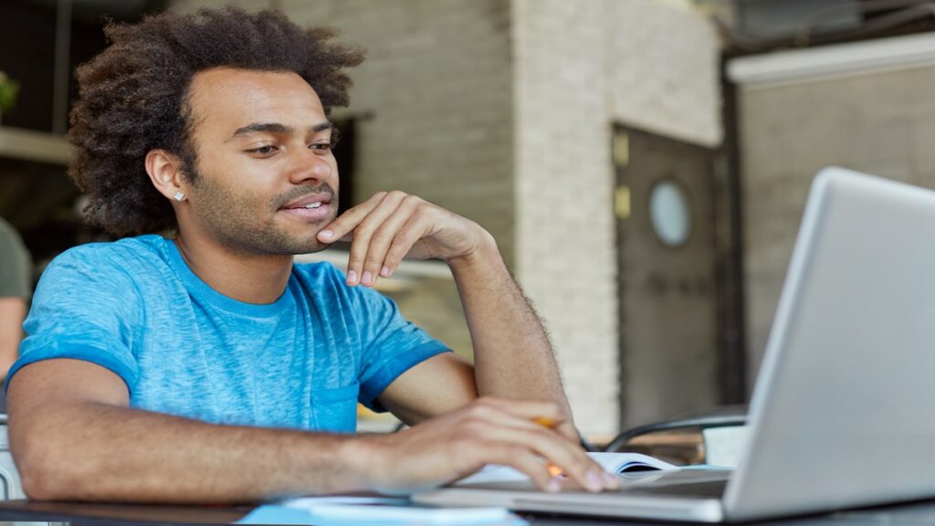 Pessoa estudando com laptop e caderno em uma mesa de tijolos à vista