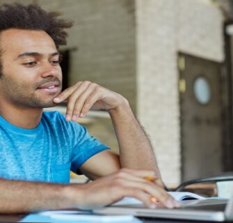Pessoa estudando com laptop e caderno em uma mesa de tijolos à vista